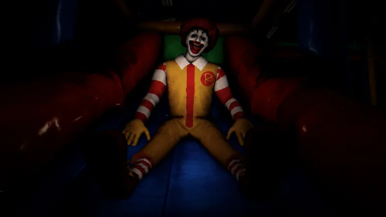 A grinning clown in a red and white striped shirt and yellow overalls sits at the foot of a red inflatable slide in a dark play area.